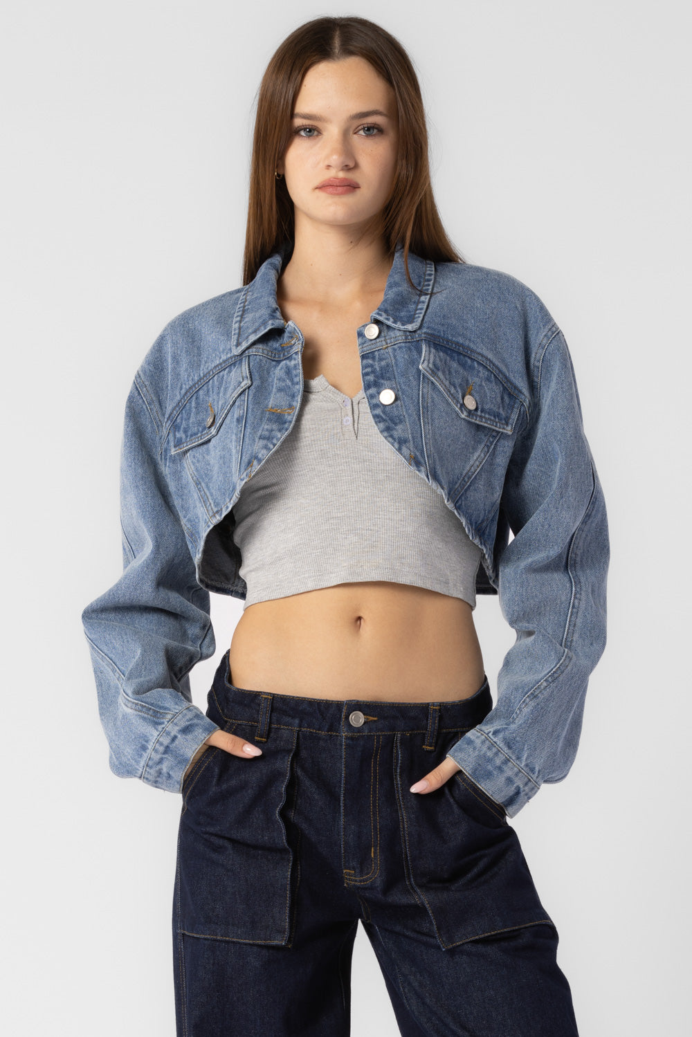 A model wearing a cropped denim jacket against a white wall. 