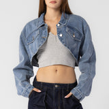 A model wearing a cropped denim jacket against a white wall. 