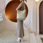 A model wearing a large tan tote bag with a knotted handle.