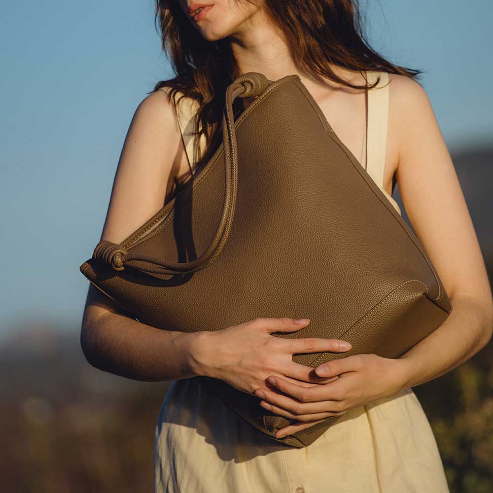 A model wearing a large vegan leather tote bag with a knotted handle.