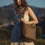 A model wearing a large vegan leather tote bag with a knotted handle while outside.