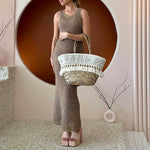 a model wearing a large straw woven tote bag with seashell detail and drawstring closure.