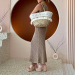 A model wearing a large straw woven tote bag with seashell details and drawstring closure.