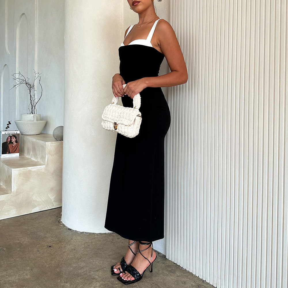 A model holding a white knitted crossbody handbag with gold clasp against a white wall. 