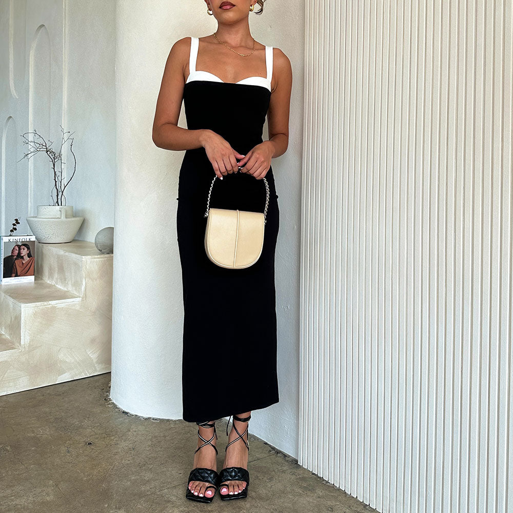 A model holding a nude vegan leather crossbody handbag against a white wall.