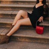 A model holding a red vegan leather crossbody handbag with silver handle. 