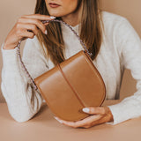 A model holding a tan vegan leather crossbody handbag with silver handle.