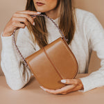 A model holding a tan crossbody  handbag with silver handle.