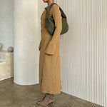 Model wearing a suede recycled vegan leather shoulder bag against a white wall. 
