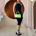 A model wearing a small lime vegan leather rectangle shaped top handle bag.
