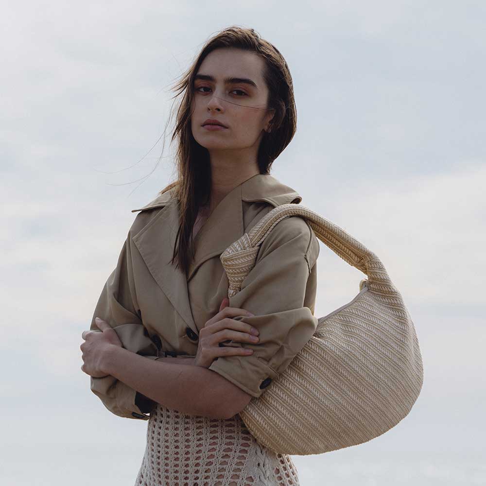 A model wearing a large natural straw woven shoulder bag with a knot handle