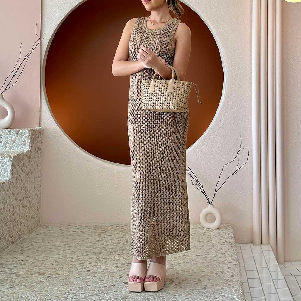 A model wearing a small nude woven vegan leather top handle bag with a drawstring closure.