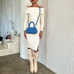 A model wearing a sky oval shaped crossbody handbag against a white wall. 