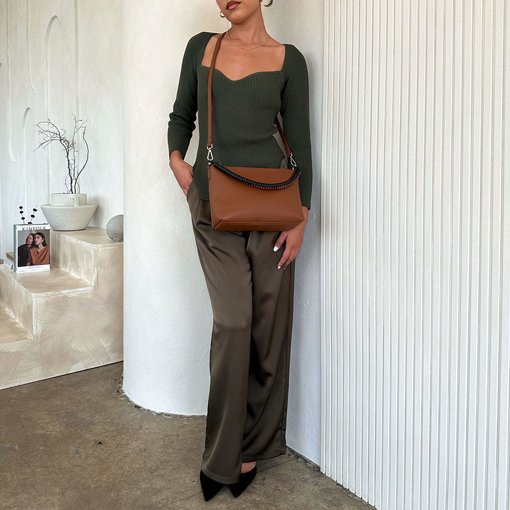 A model wearing a A small saddle recycled vegan leather crossbody bag against a white wall. 