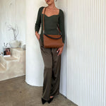 A model wearing a saddle small recycled vegan leather handbag against a white wall. 