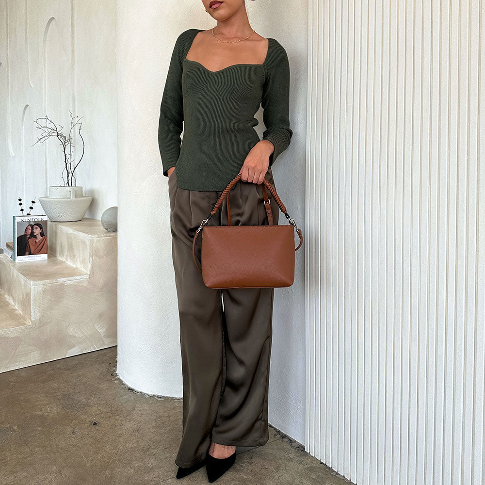A model holding a saddle small vegan leather crossbody handbag against a white wall. 