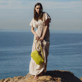 A model wearing a small lime woven vegan leather clutch with a crossbody strap while standing on rocks.