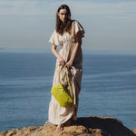 A model wearing a small woven vegan leather clutch with a crossbody strap while standing on rocks.