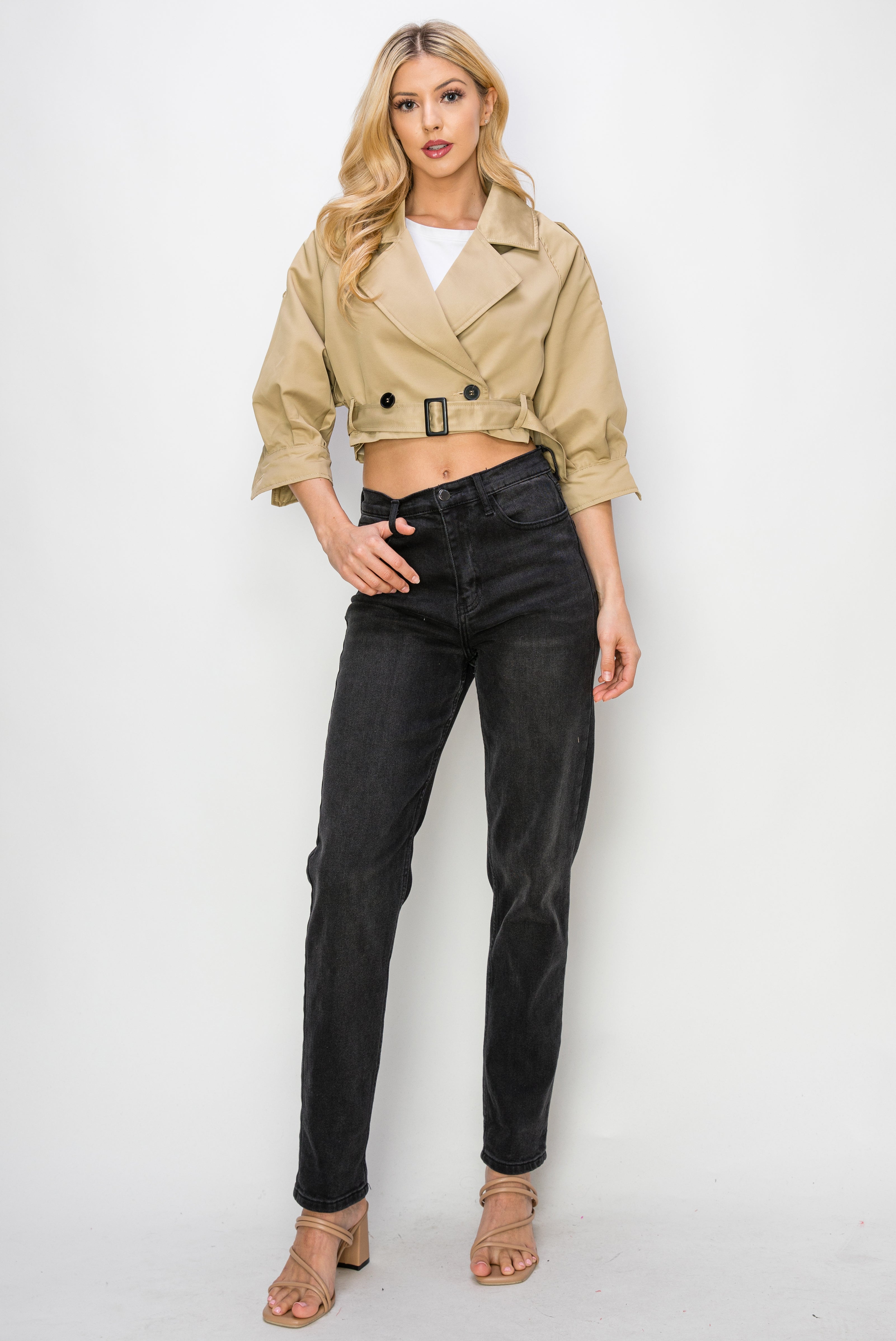 A model wearing a cropped trench jacket full body image against a white wall. 