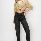 A model wearing a cropped trench jacket full body image against a white wall. 