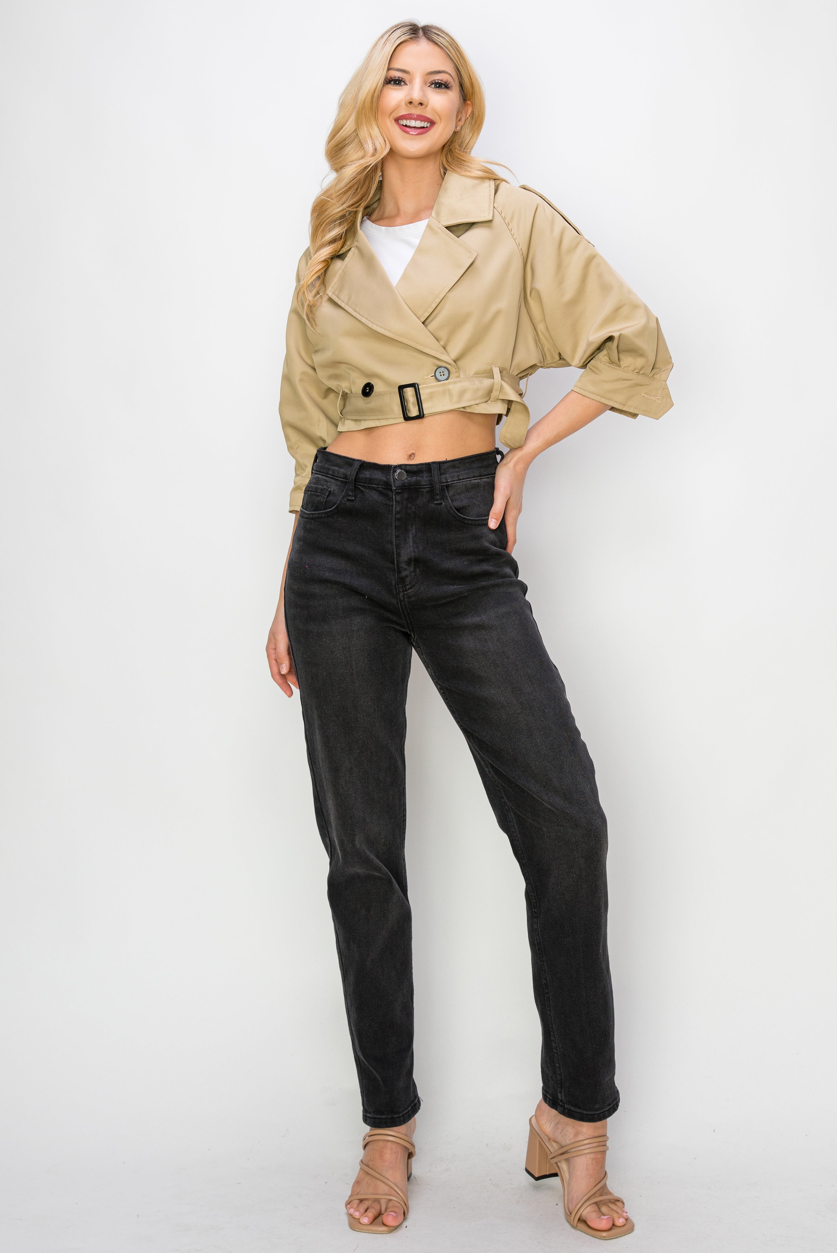 A model wearing a cropped trench jacket full body image against a white wall. 