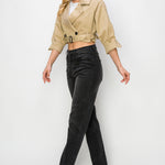 A model wearing a cropped trench jacket sideview full body image against a white wall. 