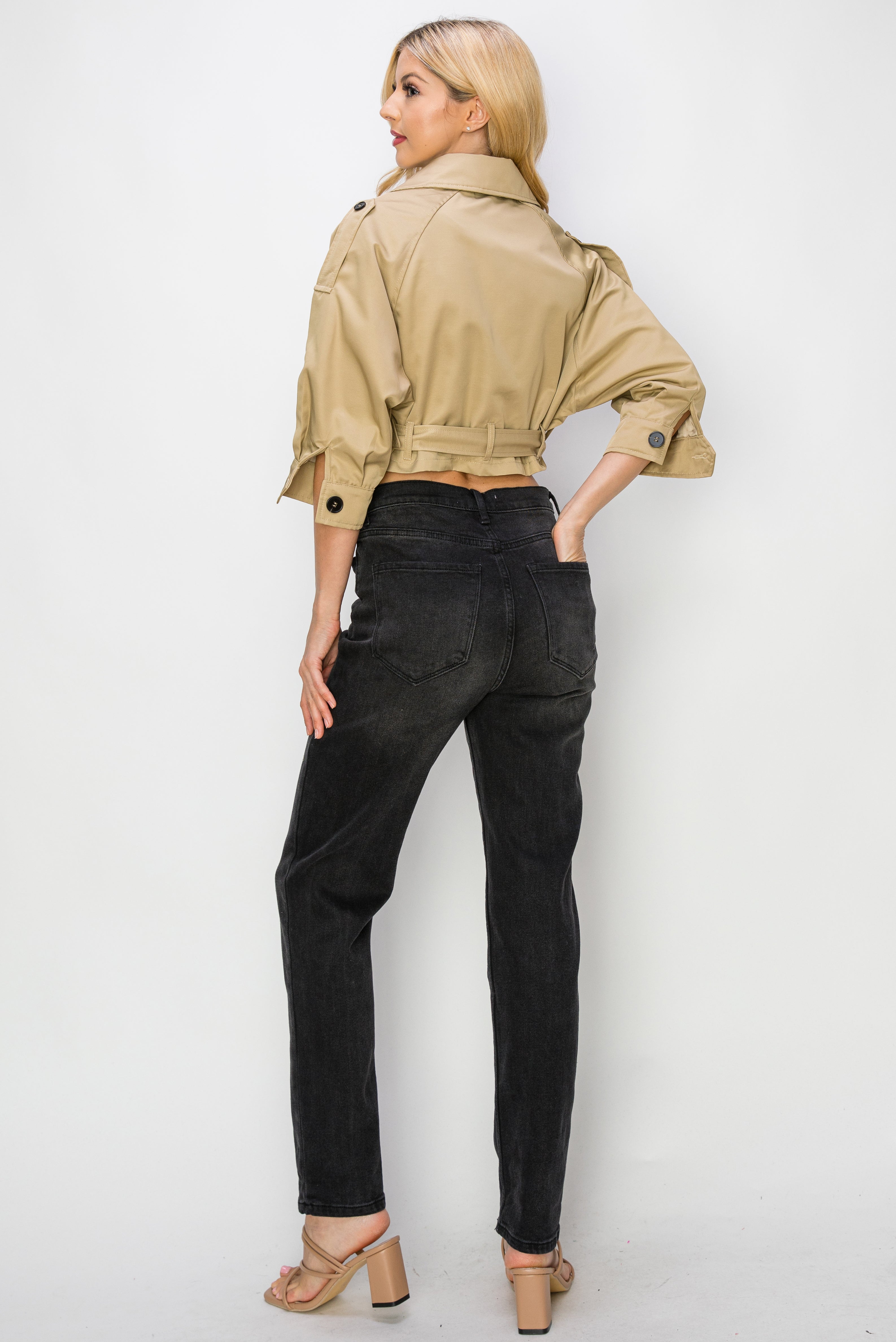 A model wearing a cropped trench jacket backside view against a white wall. 