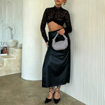 A model holding a small crystal encrusted crossbody bag against a white wall. 