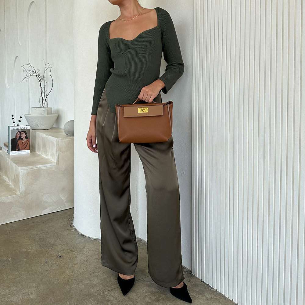 A model holding a saddle medium recycled vegan leather crossbody bag against a white wall. 