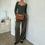 A model wearing a medium vegan leather crossbody bag against a white wall. 
