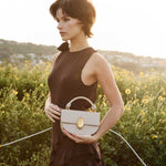 Woman holding a beige handbag in a field of yellow flowers