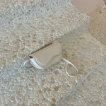 A still image of a small nude vegan leather crossbody bag with a wavy front flap closure laying against a stone background.