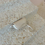 A still image of a nude vegan leather crossbody bag with a wavy front flap closure laying against a stone background.
