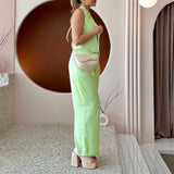 A model wearing a small nude vegan leather crossbody bag with a wavy front flap closure.