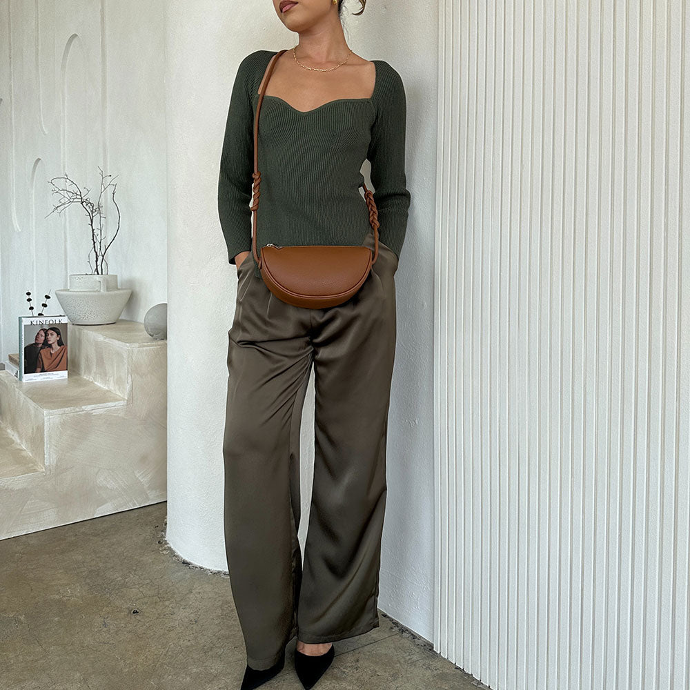 A model wearing satin straight leg pant against a white wall. 