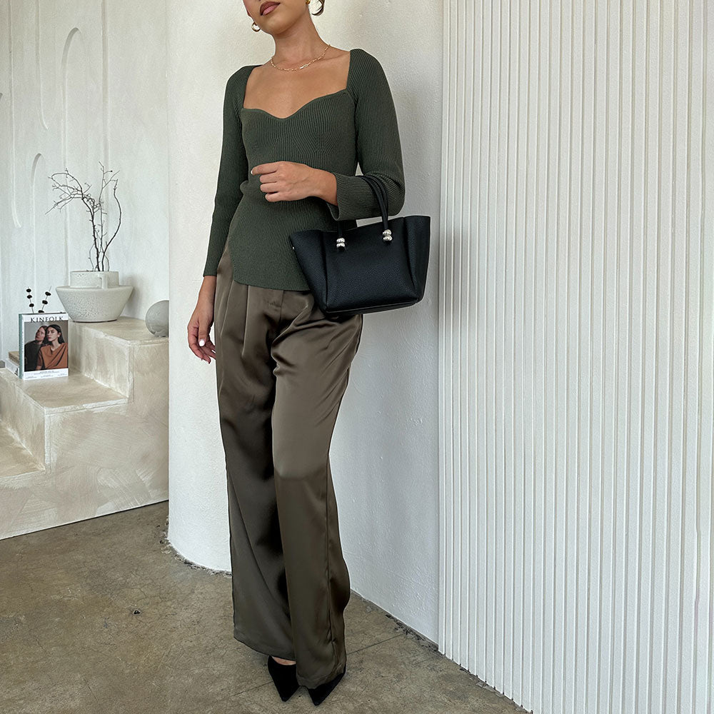 A model wearing a recycled vegan leather top handle bag against a white wall.