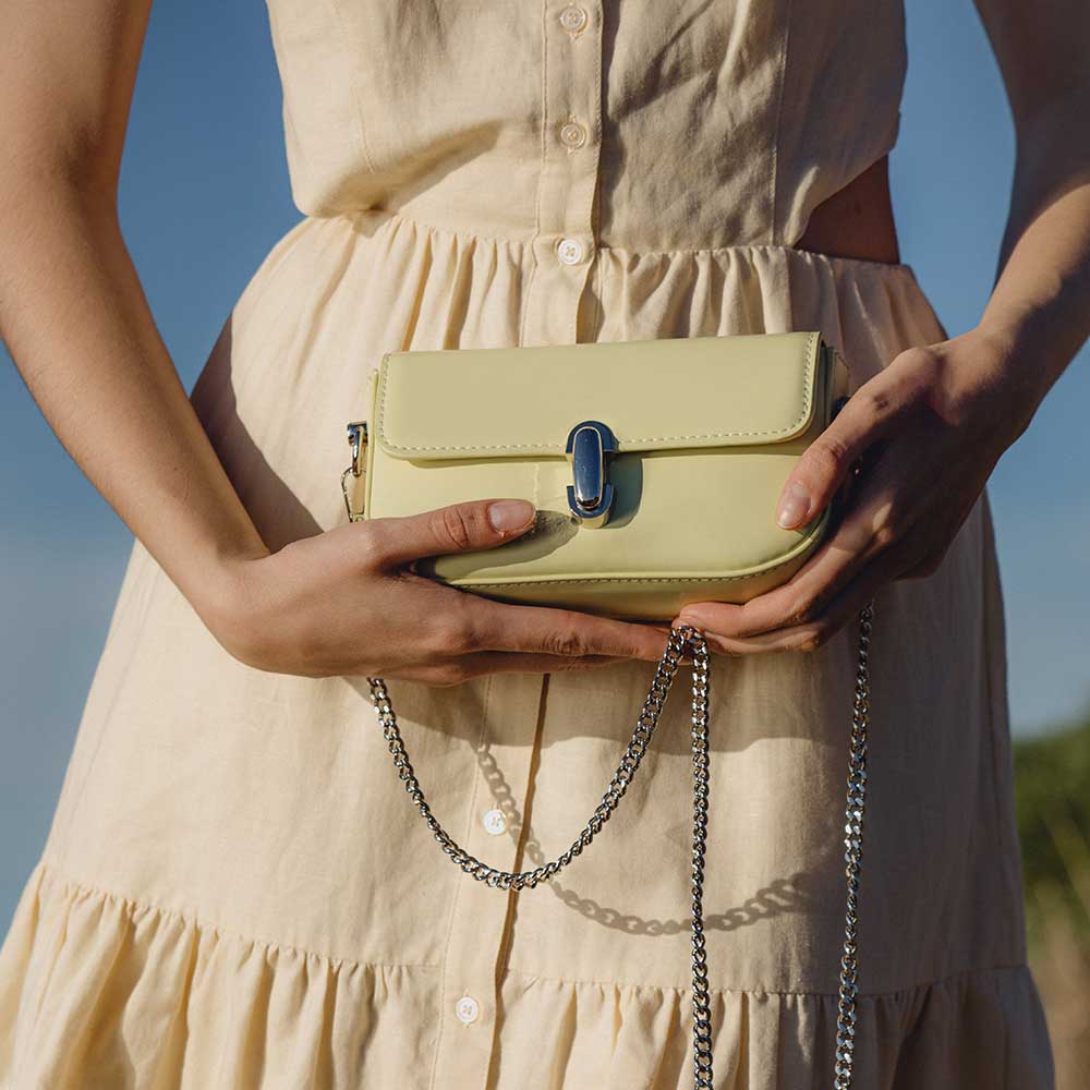 A model wearing a mini pistachio vegan leather crossbody bag with a silver clasp closure.