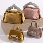 A still image of four different velvet handbags with silver encrusted handles and bows against a wooden prop.