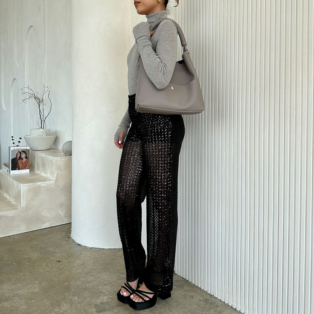 A model wearing a pebble vegan leather tote bag with a spiral handle against a white wall. 