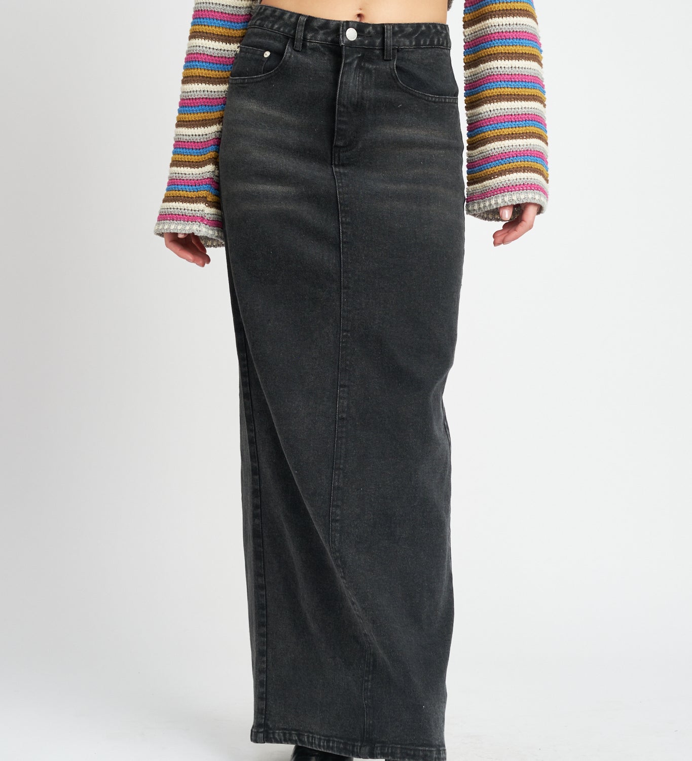 A model wearing a long black denim pencil skirt against a white wall. 