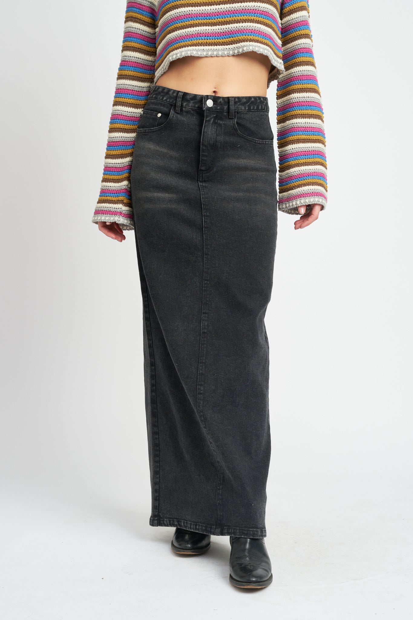 A model wearing a long black denim pencil skirt against a white wall. 