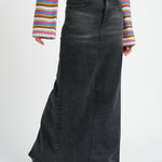 A model wearing a long black denim pencil skirt against a white wall. 