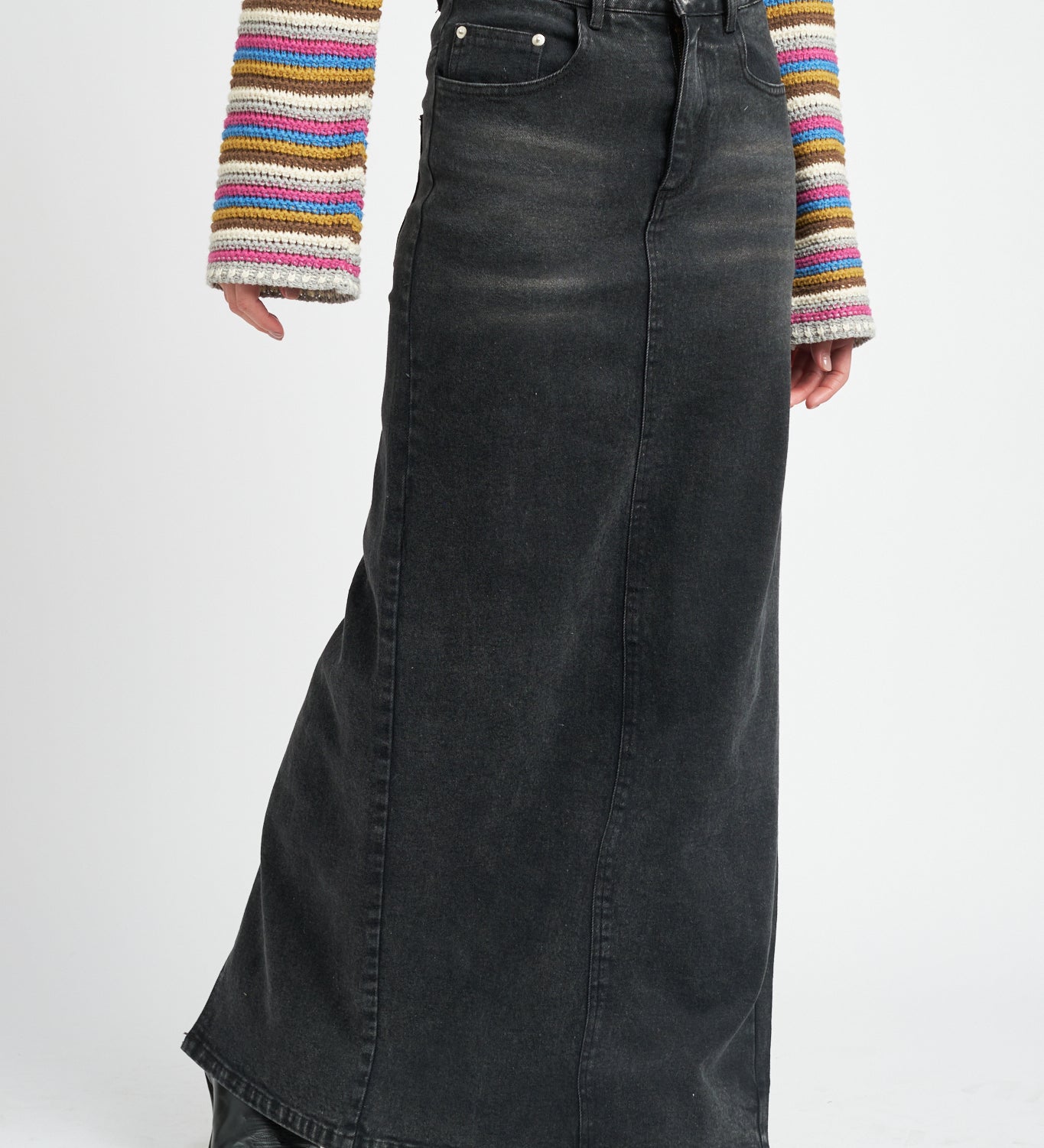 A model wearing a long black denim pencil skirt against a white wall. 