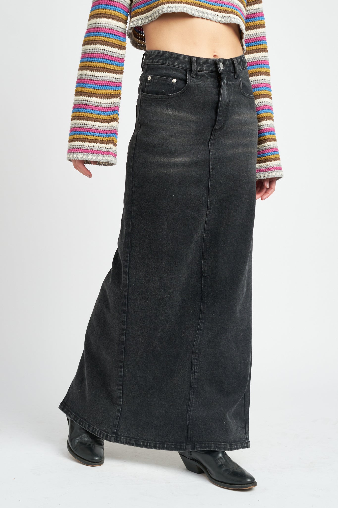 A model wearing a long black denim pencil skirt against a white wall. 