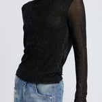 A model wearing a black rhinestone deep cowl neck backless top against a white wall. 