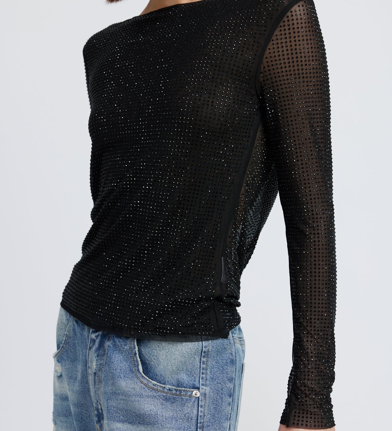 A model wearing a black rhinestone deep cowl neck backless top against a white wall. 
