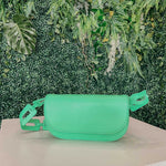 A still image of a neon green vegan leather shoulder bag with a scalloped strap against a greenery background.
