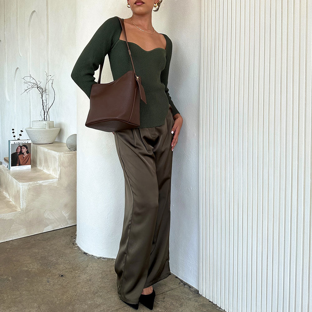 Model wearing an espresso recycled vegan leather shoulder bag against a white wall. 