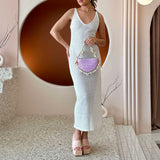 A model wearing a small lavender crochet straw top handle bag with seashell details along the handle.