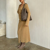 A model wearing a large woven vegan leather shoulder bag against a white wall. 